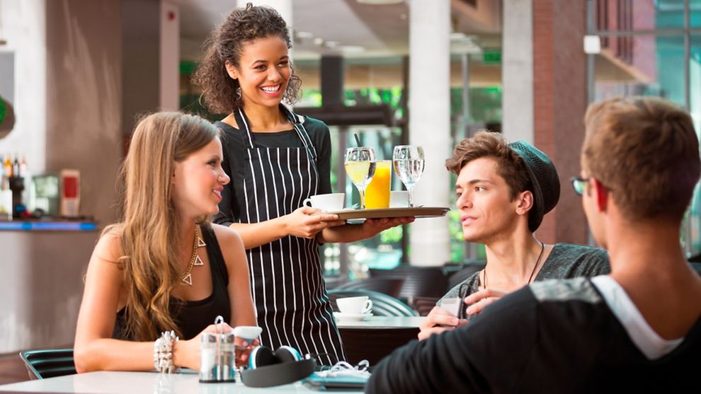 Junge Kellnerin serviert einer Gruppe Jugendlicher Getränke 